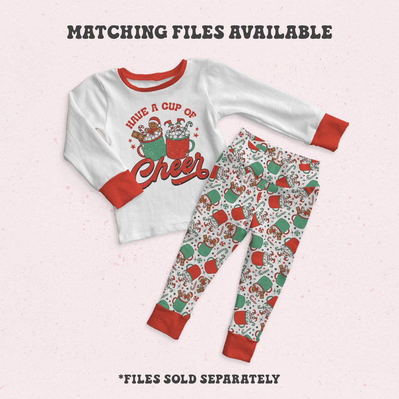 May include: White long-sleeved shirt with red trim and a graphic of two mugs of hot chocolate with marshmallows and a gingerbread man. The text "Have a cup of cheer" is printed on the shirt. White trousers with a red and green pattern of mugs of hot chocolate.