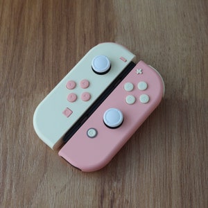 May include: A pink and white Nintendo Switch controller with white buttons and a pink and white design.