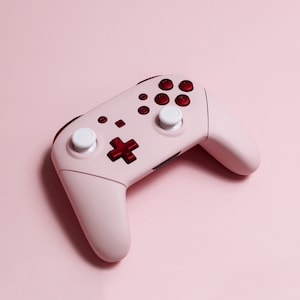 May include: A pink Nintendo Switch controller with red buttons and white analogue sticks.