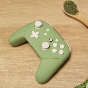 Peut inclure: Une manette de jeu vidéo verte et blanche avec un bouton en forme de croix, quatre boutons ronds et deux sticks analogiques.