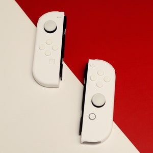 May include: Two white wireless game controllers with black buttons and a white background.