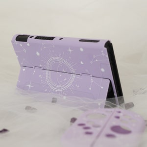 May include: A lavender purple Nintendo Switch case with a white celestial design featuring a crescent moon, stars, and constellations.