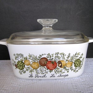 May include: White ceramic casserole dish with a glass lid. The dish has a floral design with a variety of herbs and vegetables, including parsley, sage, and tomatoes. The text "Le Persil La Sauge" is printed on the bottom of the dish.