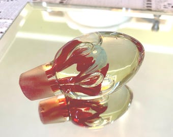 May include: A clear glass bottle stopper with a red and blue design inside. The stopper is reflected on a mirrored surface. The stopper's base is a solid red color.