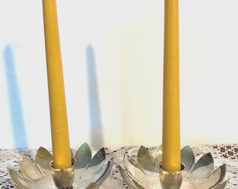 May include: Two silver lotus flower candle holders each holding a tall, yellow candle. The candle holders have a detailed petal design and sit on a decorative base. The candles are approximately 10 inches tall.