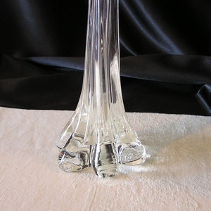 May include: A clear glass vase with a tall, slender body and a wide, flared base. The vase has a textured surface and a unique, sculptural design.