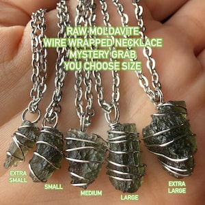 May include: Raw moldavite necklaces with wire wrapping, available in various sizes. The image shows five necklaces with green-colored moldavite stones, each with a different size, from extra small to extra large. The text on the image says "RAW MOLDAVITE WIRE WRAPPED NECKLACE MYSTERY GRAB YOU CHOOSE SIZE."