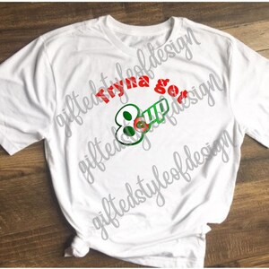 May include: White t-shirt with the text "Tryna get 8 up" in red and green lettering. The text is stylized to look like a key.