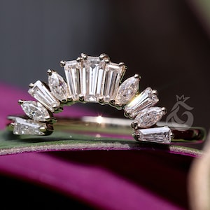 Puede incluir: Un anillo de oro con una banda curva en forma de arco, adornado con una serie de piedras transparentes alternadas en corte baguette y marquesa. Las piedras están dispuestas en forma de abanico a lo largo de la parte superior del anillo.