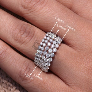 Puede incluir: Un anillo de banda de varias filas en tono plateado con cinco filas de pequeñas piedras redondas y transparentes. El anillo muestra etiquetas de medición técnicas que indican anchos de 1,70 mm, 1,90 mm, 2,10 mm, 2,30 mm y 2,50 mm.