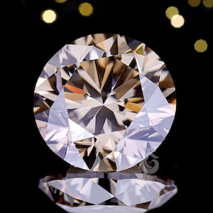 May include: A round, faceted diamond with a warm, champagne colour. The gemstone is set against a black background, with a mirrored reflection below. The diamond's many facets catch and reflect light, creating a sparkling effect.