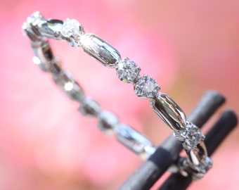 May include: A silver-toned ring featuring an alternating pattern of small, round, clear faceted stones and smooth, elongated metallic bars. The band is held in place by a dark, thin, cylindrical tool, showcasing the intricate metalwork and stones.