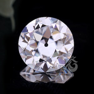 May include: A round, colorless, faceted gemstone with a brilliant cut, featuring a distinct culet at the center. The stone displays sharp geometric facets that reflect light, creating a clear, sparkling appearance against a dark background.