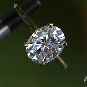 Pu&ograve; includere: Primo piano di un anello di diamanti ovale scintillante incastonato in una fascia d'oro.