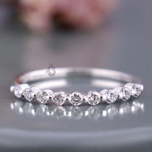 May include: A silver-toned band ring featuring a row of nine small, round, clear stones set in a shared-prong setting. The metal has a polished, reflective finish, and the stones are arranged horizontally across the front of the band.