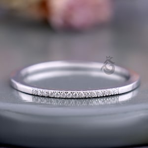 May include: A slender silver ring featuring a line of tiny, glittering gemstones. The ring has a polished finish and a delicate design. The gemstones are clear and evenly spaced, adding a subtle sparkle. The ring's design is elegant and refined.