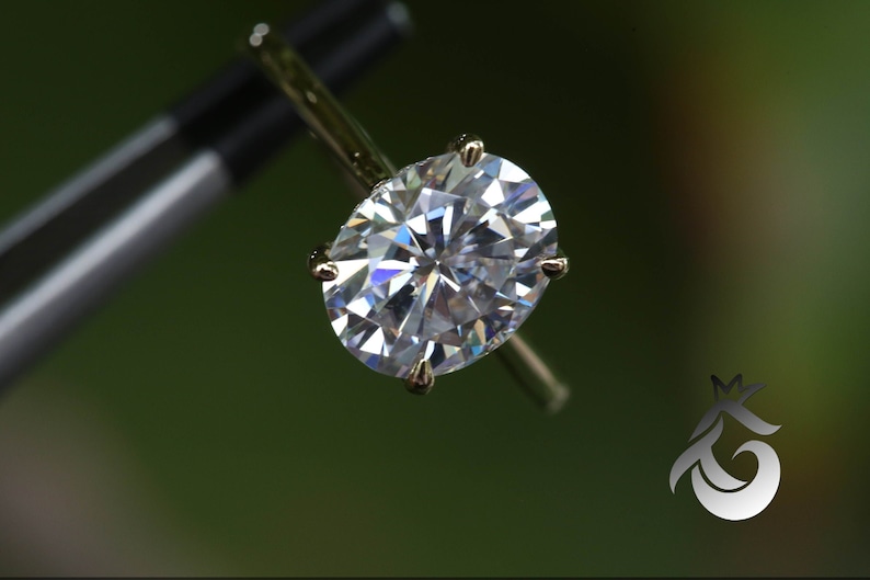 Pu&ograve; includere: Primo piano di un anello di diamanti ovale scintillante incastonato in una fascia d'oro.
