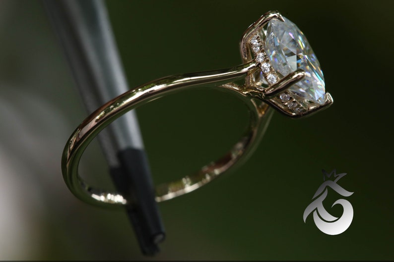 Pu&ograve; includere: Un anello d'oro con una grande pietra ovale trasparente circondata da un alone di pietre pi&ugrave; piccole.