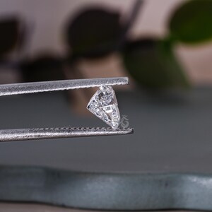 May include: A clear, faceted, triangular diamond gemstone held in tweezers.