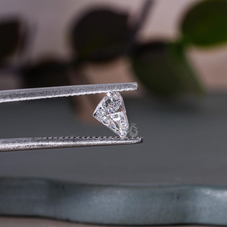 May include: A clear, faceted, triangular diamond gemstone held in tweezers.