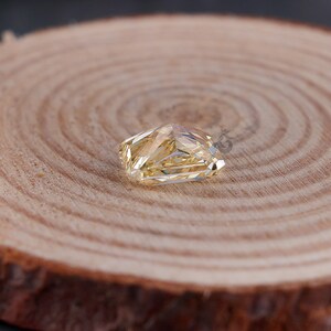 May include: A radiant-cut, pale yellow gemstone with a faceted surface that reflects light. The stone has a rectangular shape with clipped corners and a transparent, crystalline appearance, showcasing intricate geometric patterns within its structure.