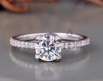 Könnte beinhalten: Ein silberfarbener Ring mit einem großen, runden, im Brillantschliff geschliffenen Mittelstein, der von vier Krappen gehalten wird. Die Ringschiene ist schmal und auf beiden Seiten mit einer Reihe kleiner, klarer Steine besetzt.