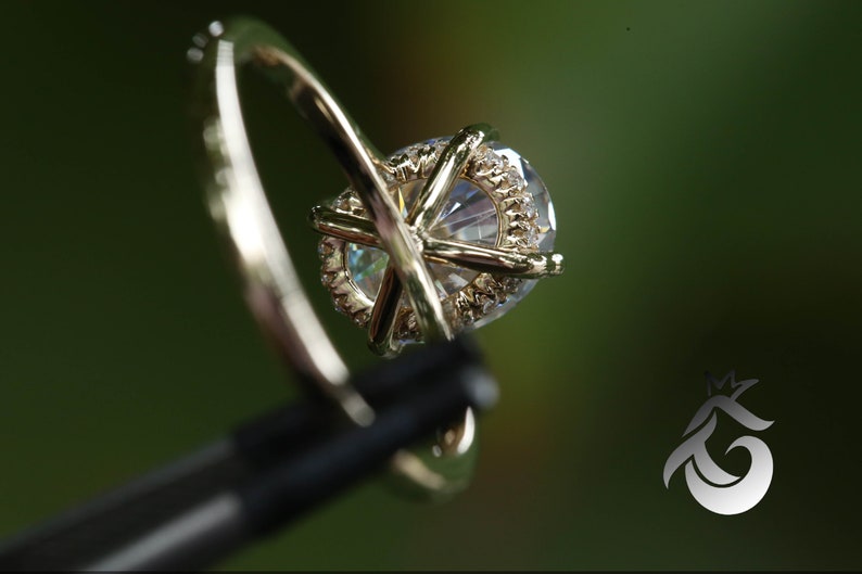 Pu&ograve; includere: Un anello di fidanzamento in oro con un grande diamante centrale di forma ovale circondato da un alone di diamanti pi&ugrave; piccoli. L'anello &egrave; incastonato su una fascia sottile con una montatura pav&eacute;.