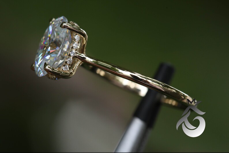 Pu&ograve; includere: Un anello di fidanzamento in oro con un grande diamante centrale di forma ovale e diamanti pi&ugrave; piccoli incastonati in un alone attorno al diamante centrale.