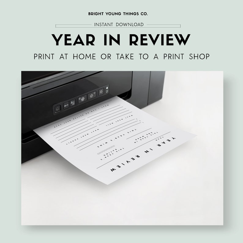 May include: A black and white printable year in review planner sheet is being printed from a black printer. The sheet has lines for writing and the text "YEAR IN REVIEW" is printed at the top and bottom of the sheet.