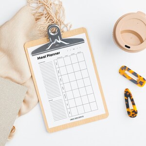 May include: A white meal planner on a clipboard with a wooden frame. The planner has sections for shopping, notes, and a weekly meal plan with columns for breakfast, lunch, dinner, and snacks.