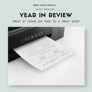 May include: A black printer printing a white "Year in Review" printable sheet. The sheet has prompts for reflection, including "This Year's Wins" and "What Went Well." The text "Bright Young Things Co." and "Instant Download" are at the top.