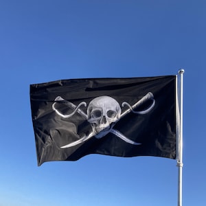 Peut inclure: Un drapeau de pirate noir avec un motif de crâne et d'os croisés blancs. Le crâne a une structure faciale détaillée et les os croisés sont formés par deux épées.