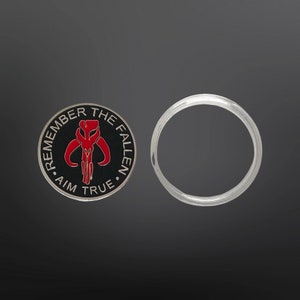 May include: A black and silver coin with a red Mandalorian symbol and the text "Remember the Fallen - Aim True".