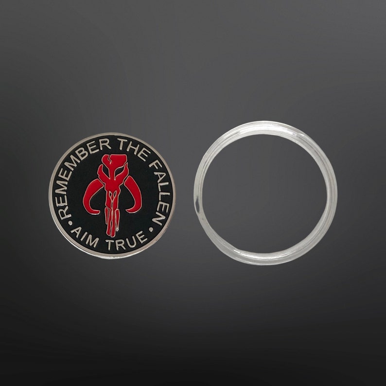 May include: A black and silver coin with a red Mandalorian symbol and the text "Remember the Fallen - Aim True".