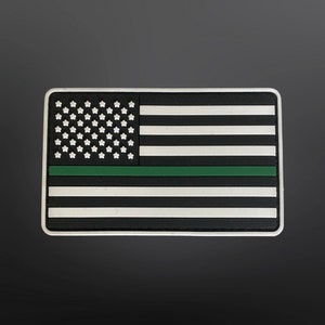 Könnte beinhalten: Ein schwarz-weißes amerikanisches Flaggen-Patch mit einem grünen Streifen in der Mitte. Die Flagge ist aus einem strukturierten Material gefertigt und hat einen weißen Rand.