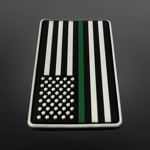Op de afbeelding: Een zwart-witte Amerikaanse vlagpatch met een groene streep in het midden. De patch is gemaakt van duurzaam materiaal en is perfect om een ​​patriotische touch aan je bezittingen toe te voegen.