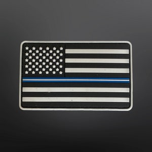 May include: A black and white American flag patch with a thin blue line across the middle. The patch is made of rubber and has a white border.
