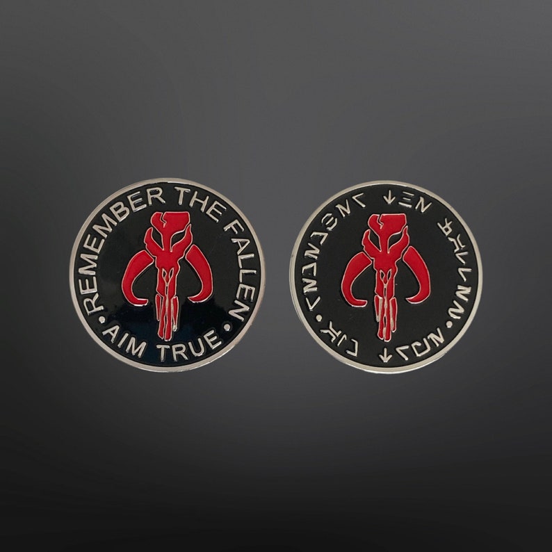 May include: Two black and silver Mandalorian symbol coins with red accents. One coin reads "Remember the Fallen Aim True" and the other reads "Live for the Fallen Aim True".