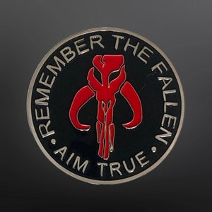 May include: A silver and black round coin with a red Mandalorian symbol and the text "Remember the Fallen. Aim True."