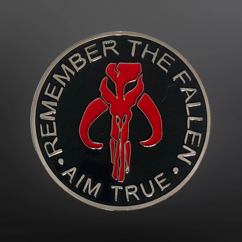 May include: A silver and black round coin with a red Mandalorian symbol and the text "Remember the Fallen. Aim True."