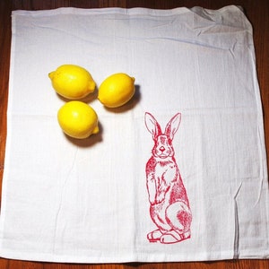 Puede incluir: Pa&ntilde;o de cocina blanco con una ilustraci&oacute;n de conejo rojo y tres limones amarillos. El conejo est&aacute; de pie. Los limones est&aacute;n agrupados en el lado izquierdo del pa&ntilde;o.