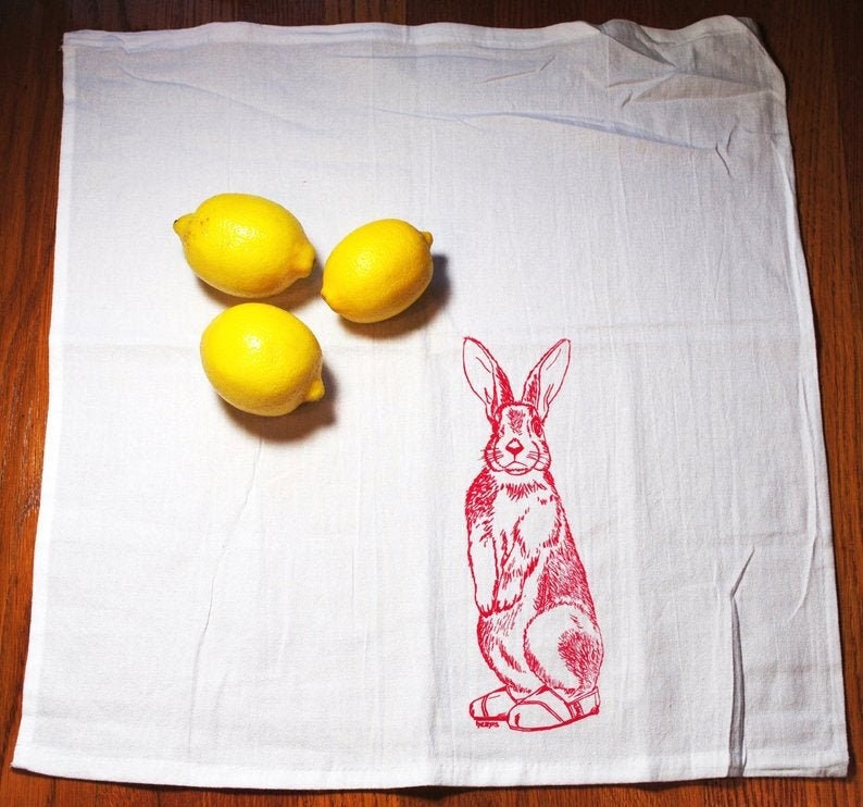 Puede incluir: Pa&ntilde;o de cocina blanco con una ilustraci&oacute;n de conejo rojo y tres limones amarillos. El conejo est&aacute; de pie. Los limones est&aacute;n agrupados en el lado izquierdo del pa&ntilde;o.