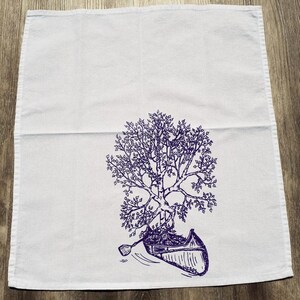 Pode incluir: Uma toalha de cozinha branca com uma ilustra&ccedil;&atilde;o de tinta roxa de uma &aacute;rvore crescendo em uma canoa. A canoa est&aacute; na &aacute;gua e h&aacute; um remo na &aacute;gua.