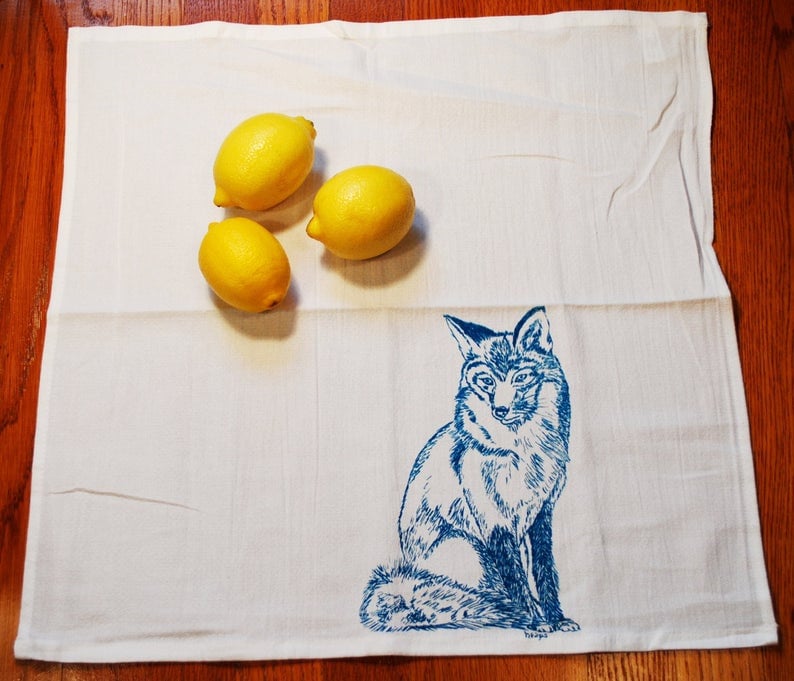 Puede incluir: Pa&ntilde;o de cocina blanco con una ilustraci&oacute;n de zorro azul y tres limones amarillos. El zorro est&aacute; representado con detalle. Los limones a&ntilde;aden un toque de color brillante.