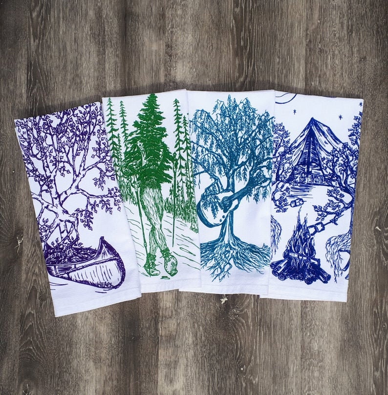 Pode incluir: Conjunto de cinco toalhas de cozinha com designs inspirados na natureza. As toalhas s&atilde;o brancas com ilustra&ccedil;&otilde;es azuis, verdes e roxas de &aacute;rvores, uma canoa, uma fogueira e um viol&atilde;o.