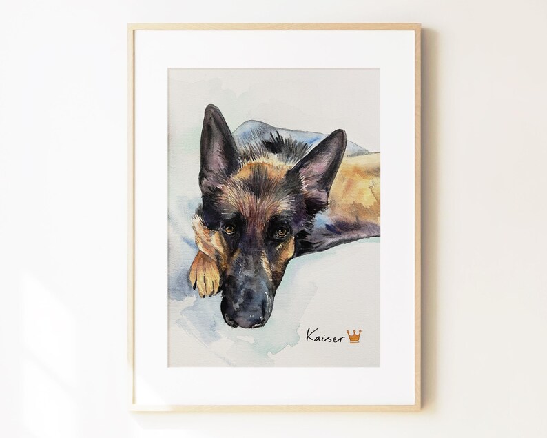 May include: A framed watercolor painting of a German Shepherd dog looking forward with black and tan fur. The name Kaiser is written in black script below the dog, accompanied by a small orange crown icon, all set against a light background.