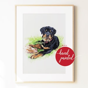 May include: A framed watercolor painting of a black and tan Rottweiler puppy lying on green grass with a leaf in its mouth. The puppy wears a red collar. A red circular stamp on the lower right corner features the text Original hand painted.
