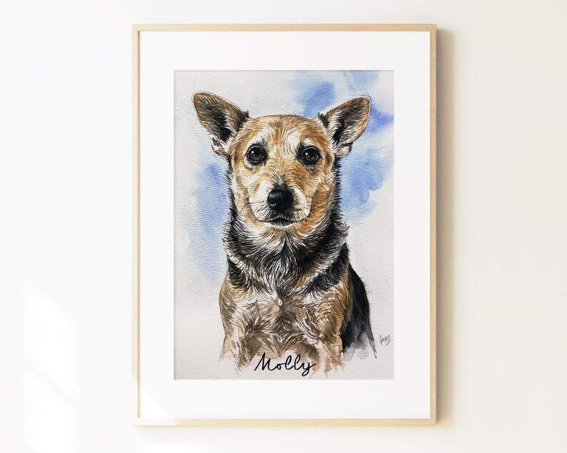 May include: A framed watercolor portrait of a brown and black dog with pointed ears, set against a soft blue wash background. The name Molly is written in black cursive script at the bottom center of the artwork, which is encased in a light wood frame.