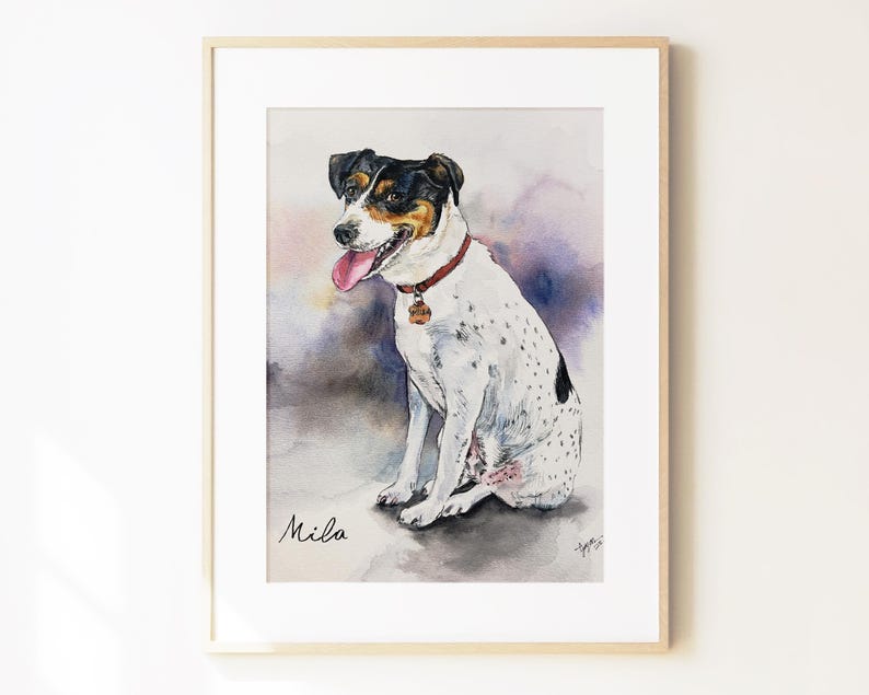 May include: A framed watercolor painting of a white dog with black and tan markings on its head, wearing a red collar with a tag. The dog is sitting with its tongue out. The name Mila is written in black script in the bottom left corner.