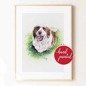 May include: A framed watercolour portrait of a brown and white dog with a happy expression, set against a green grassy background. The name Toby is written below the dog, and a red circular stamp reads Original hand painted in white text.